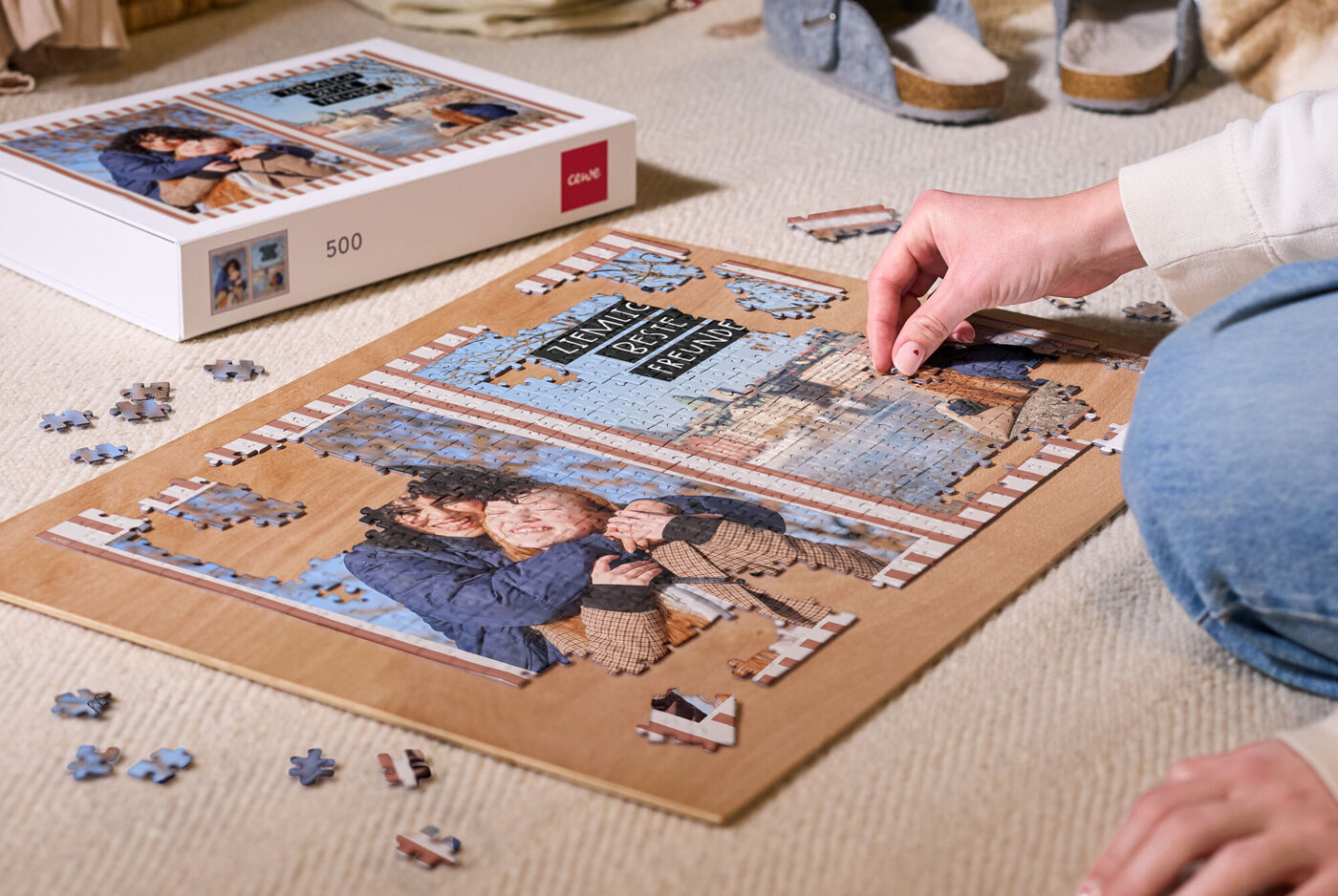 Eine Person fügt Teile in ein auf dem Boden liegenden Puzzle ein. Als Motiv ist eine Collage aus Familien- und Urlaubsfotos zu erkennen