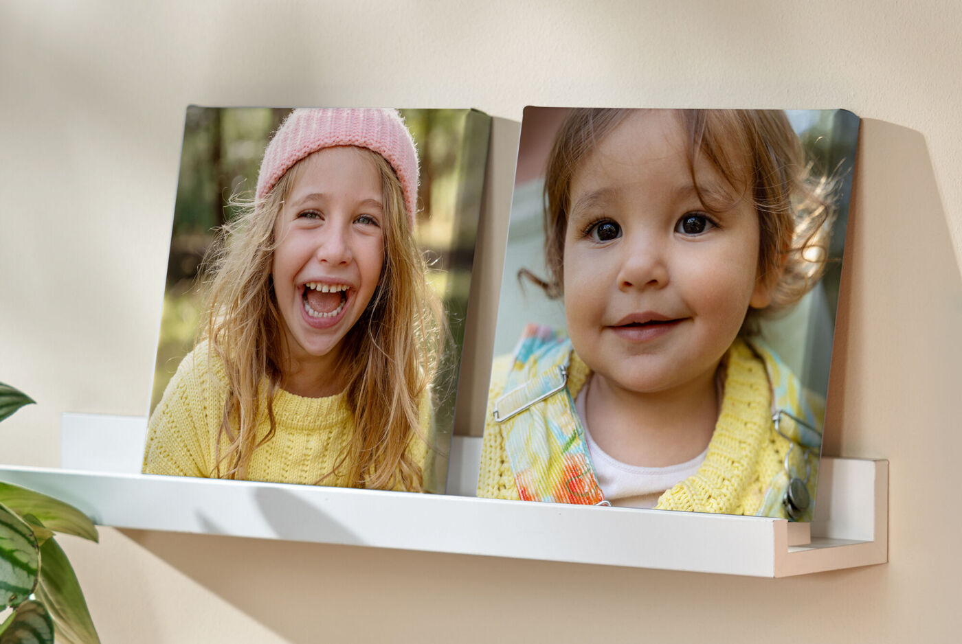 Zwei quadratische Leinwände mit Kinderfotos stehen auf einem Wandregal