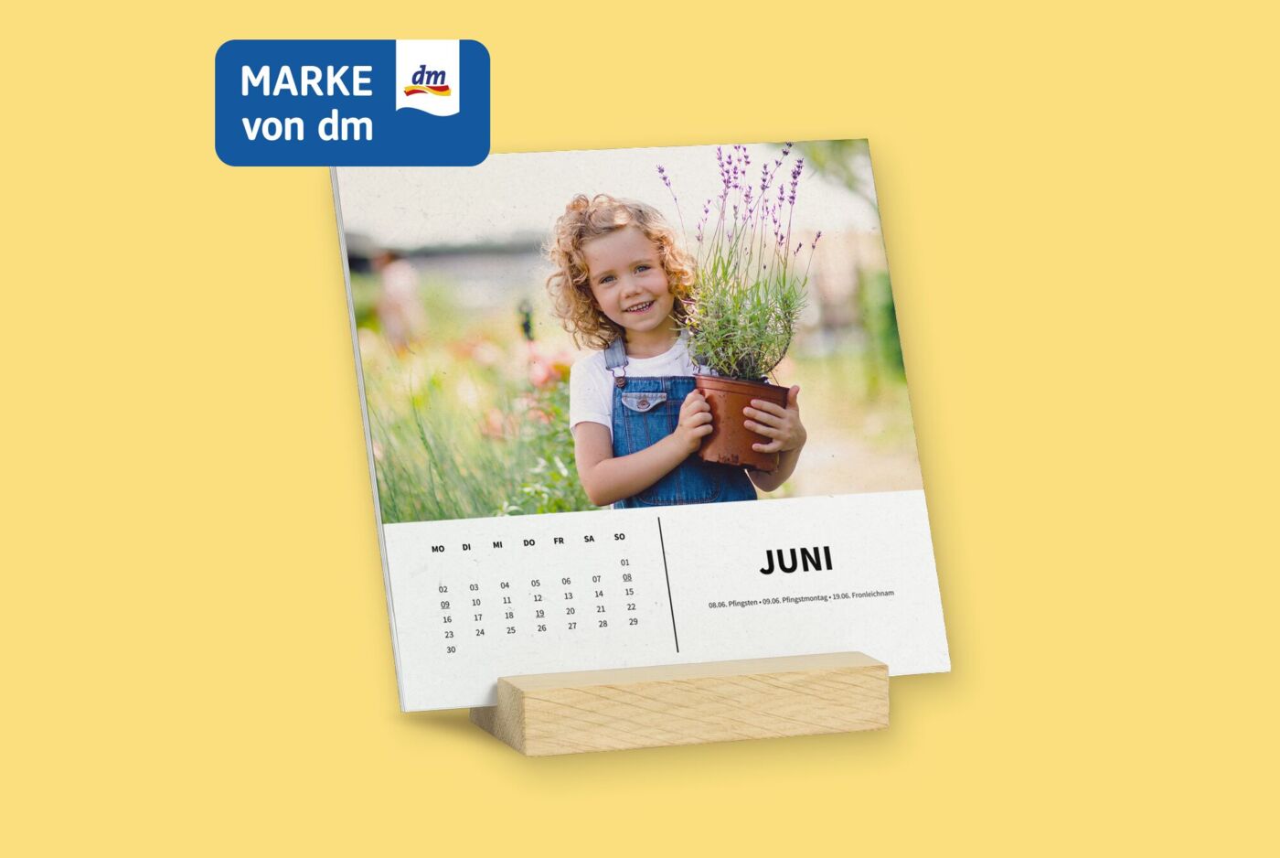 Quadratische Kalenderblätter stehen frei in einem Holzstandfuß, Kalender hat weißes Design, mit Foto von Mädchen mit Pflanze.