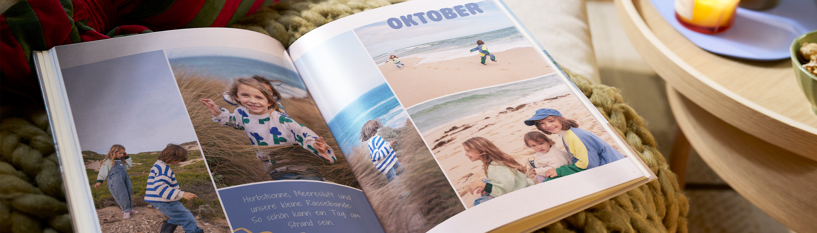 Ein aufgeschlagenes Fotobuch liegt auf einem Sofa. Die Doppelseite zeigt eine Collage mit Kinderfotos an einem Strand im Oktober
