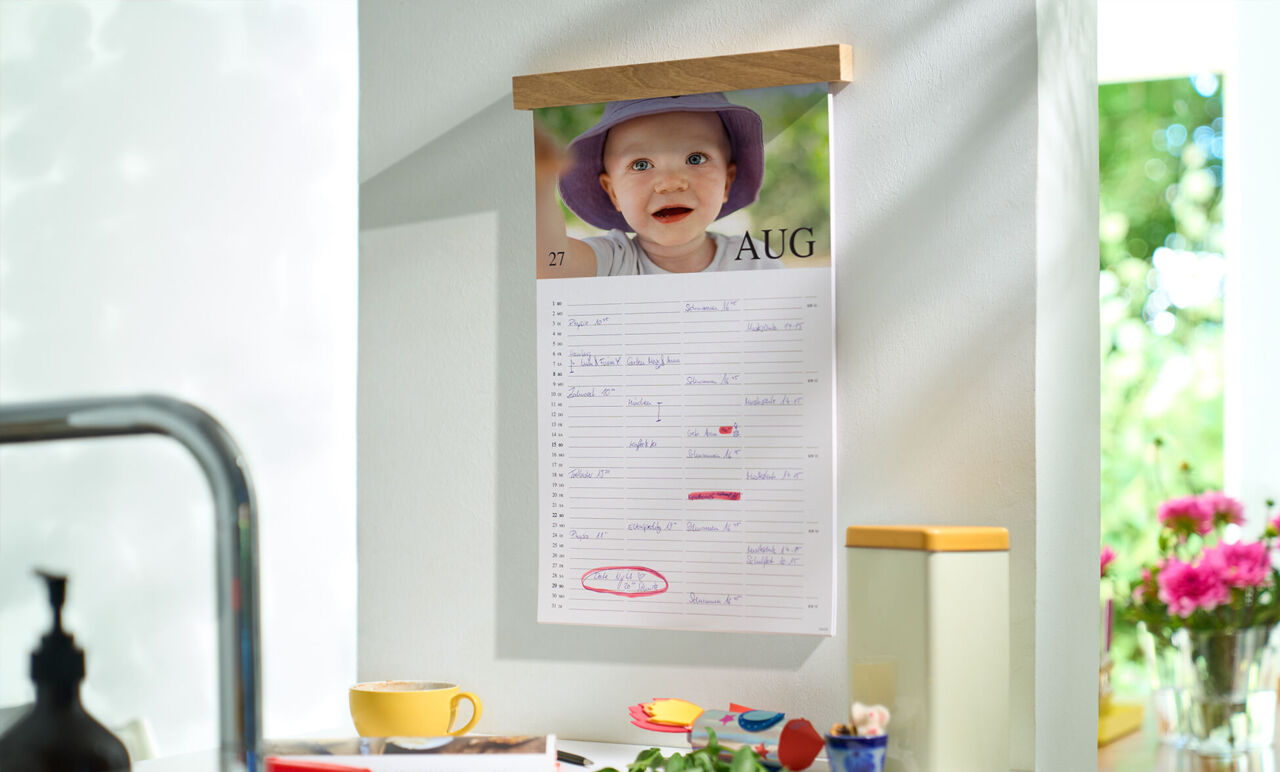 Wandkalender mit Holzleiste und Kinderfoto für den Monat August, mit Einträgen und Spalten für Familienmitglieder