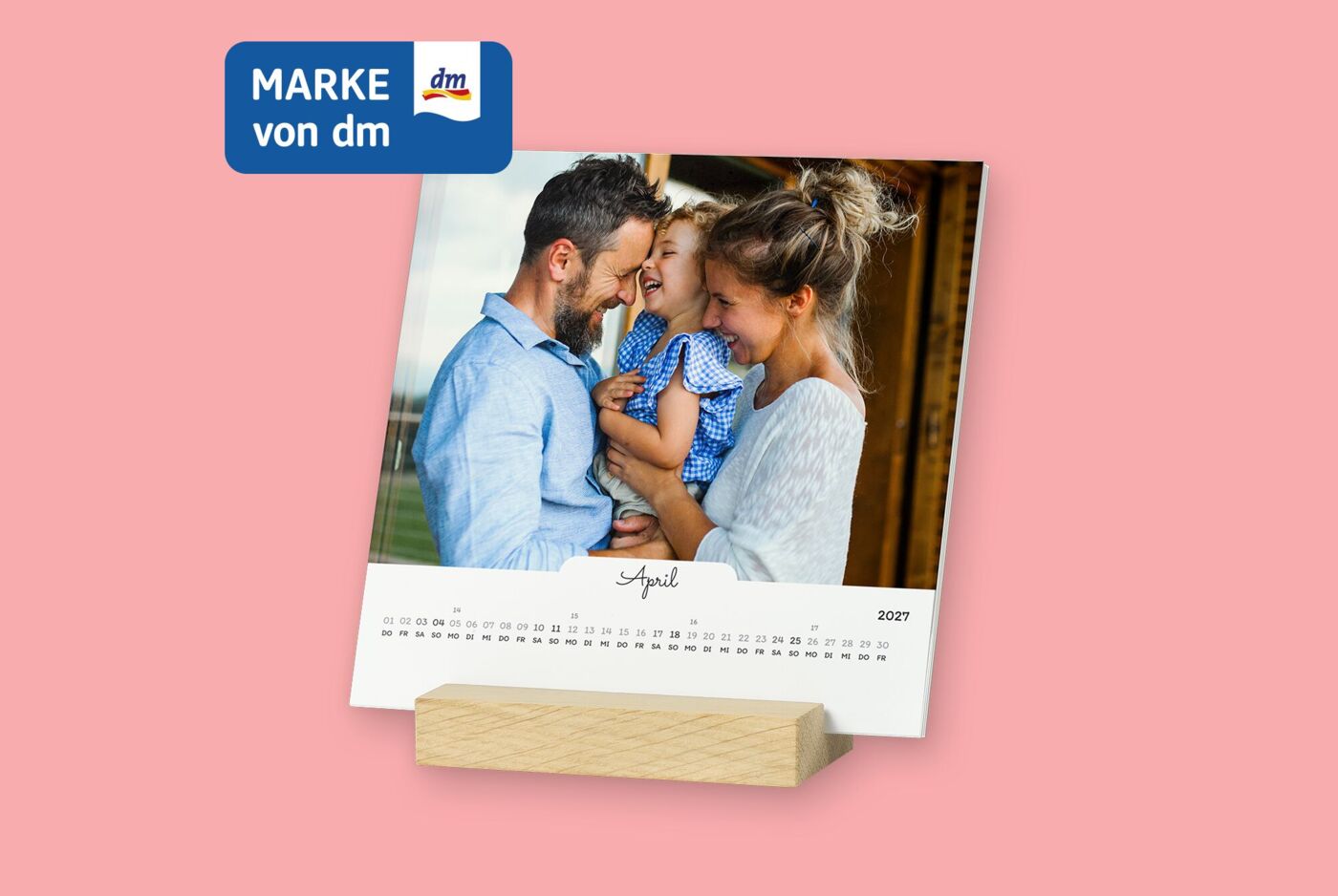 Quadratische Kalenderblätter stehen frei in einem Holzstandfuß. Kalender hat weißes Design, mit Familienfoto.