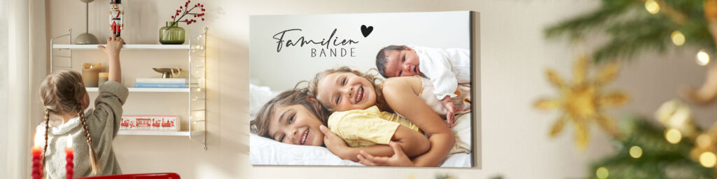 Eine Leinwand hängt an einer Wand zwischen einem Regal und einem Weihnachtsbaum. Sie zeigt ein Kinderfoto und die Überschrift: Familienbande