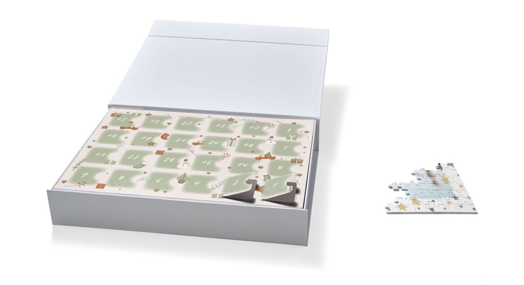 Adventskalender mit weihnachtlichem Türchendesign in einer aufgeklappten Klappbox. Zwei Türchen sind geöffnet, daneben liegen Puzzleteile