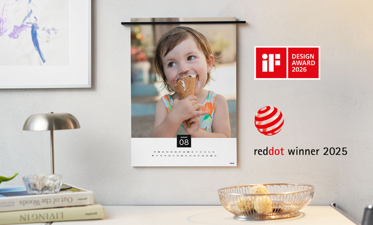 Wandkalender mit dünner Metallleiste als Aufhängung und Foto eines Kindes, das ein Eis isst. Daneben das Logo "reddot winner 2025".