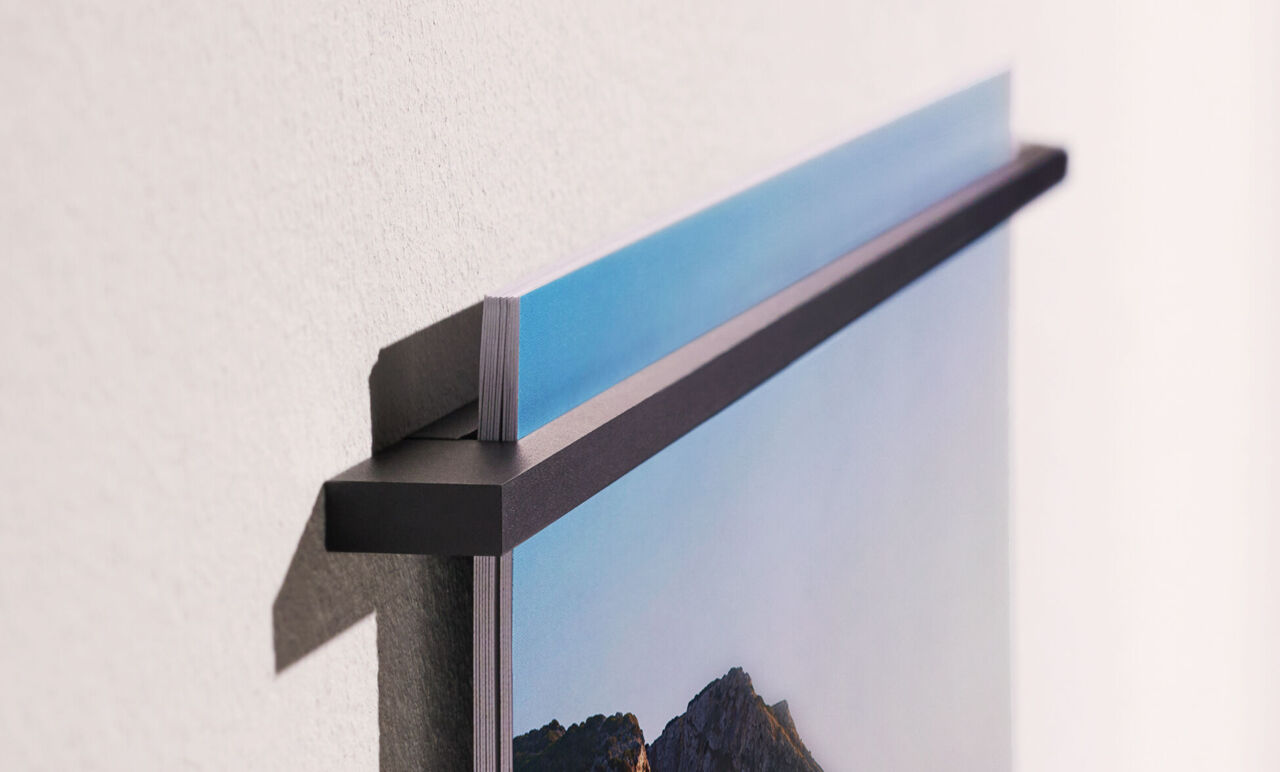 Nahaufnahme der schwarzen Metallleiste, die an einer weißen Wand befestigt ist und die einzelnen Kalenderblätter hält.